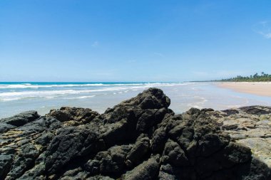 Açık gökyüzüne karşı mavi suları ve karanlık kayaları olan güzel bir sahil manzarası. Itacare, Brezilya.