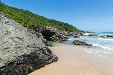 Açık gökyüzüne karşı mavi suları ve karanlık kayaları olan güzel bir sahil manzarası. Itacare, Brezilya.