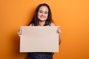 Güzel siyah saçlı Latin Amerikalı kadın elinde kendine güvenen, ayakta duran boş bir pankart tutuyor. Hardal renginde arkaplanda izole.