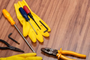 Bir çift temizlik eldiveni, pense, tornavida, ingiliz anahtarı ve ahşap arka planda izole edilmiş diğer aletler..