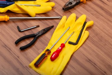 Bir çift temizlik eldiveni, pense, tornavida, ingiliz anahtarı ve ahşap arka planda izole edilmiş diğer aletler..