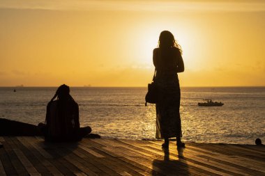 Salvador, Bahia, Brazil - December 21, 2019: Two people in silhouette are seen enjoying the sunset at the port of Barra in Salvador, Bahia. clipart