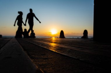 Salvador, Bahia, Brezilya - 22 Ekim 2024: İnsanlar, siluet içinde, Salvador, Bahia şehrinde Porto da Barra güvertesinde günbatımının keyfini çıkarırken görülüyor..