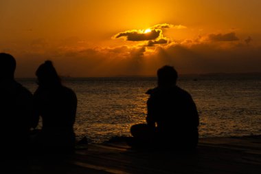 Salvador, Bahia, Brezilya - 22 Ekim 2024: İnsanlar, siluet içinde, Salvador, Bahia şehrinde Porto da Barra güvertesinde günbatımının keyfini çıkarırken görülüyor..