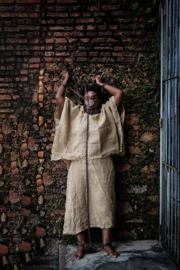 Kollarını tuğla duvara dayamış, ağzında demir bir maskeyle zincirlenmiş siyah bir kadının portresi. Brezilya 'da kölelik. Köle Anastacia 'nın temsilcisi.