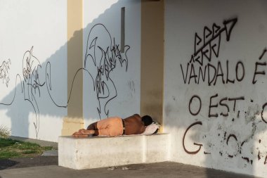 Salvador, Bahia, Brezilya - 16 Kasım 2019: Salvador, Bahia 'da bir duvarın yanındaki kilisede çimento bir bankta uyuyan bir adam görülüyor.