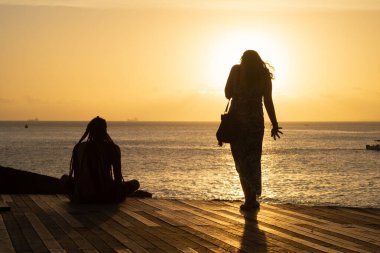 Salvador, Bahia, Brazil - December 21, 2019: Unidentified people in silhouette are seen enjoying the sunset at the port of Barra in Salvador, Bahia. clipart