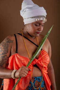Salvador, Bahia, Brezilya - 21 Ekim 2024: Geleneksel Candomble elbiseli kadın, Espada de Sao Jorge bitkisini tutuyor ve fotoğraf için poz veriyor. Salvador, Bahia.