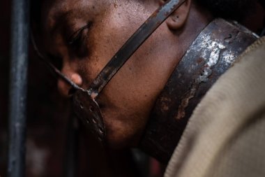 Ağzına demir bir maske takmış, demir bir çite yaslanmış siyah bir kadının yakın plan portresi. Brezilya 'da kölelik. Köle Anastacia 'nın temsilcisi.