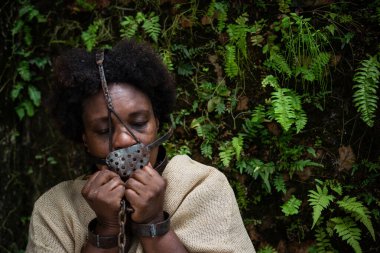 Ağzında ve boynunda demir bir maskeyle köle gibi giyinmiş ve ellerini tutan bir kadının portresi. Brezilya 'da kölelik. Köle Anastacia 'nın temsilcisi.