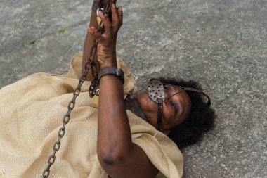 Köle gibi giyinmiş siyah bir kadın, yere zincirlenmiş, ağzında ve boynunda demir bir maskeyle ellerini kaldırıyor. Brezilya 'da kölelik. Köle Anastacia 'nın temsilcisi.