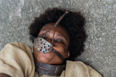 Ağzı ve boynunda demir bir maskeyle yerde acı içinde yatan siyah bir kadının yakın plan portresi. Brezilya 'da kölelik. Köle Anastacia 'nın temsilcisi.