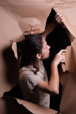 Kahverengi bir kağıt parçasındaki delikten bakan bir adam. Gazeteyi elleriyle yırttı. Stüdyo resmi.