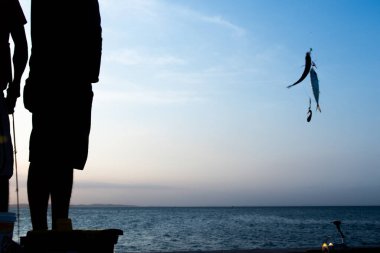 Salvador, Bahia, Brezilya - 16 Kasım 2019: Balıkçı, siluet içinde, gün batımında balık kancasıyla Salvador, Bahia 'da görüldü..