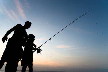 Salvador, Bahia, Brezilya - 16 Kasım 2019: Silhouette 'de bir adam ve çocuk, gün batımında Bahia' nın Salvador kentinde balık tutarken görüldü..