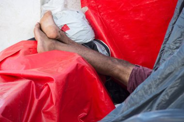 Kimliği belirsiz birinin ayakları ve bacakları bir şilte ve plastiğin üzerinde uyuyor. Evsiz insanlar. Salvador, Brezilya.