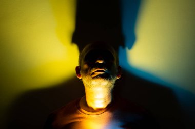 Beyaz adam, üzerinde mavi ve sarı renkli ışıklar olan bir duvara yaslanmış fotoğraf için poz veriyor. Stüdyo portresi. Flaş sanat.