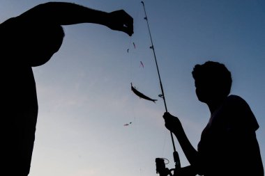 Salvador, Bahia, Brezilya - 16 Kasım 2019: Silhouette 'de bir adam ve çocuk, gün batımında Bahia' nın Salvador kentinde balık tutarken görüldü..