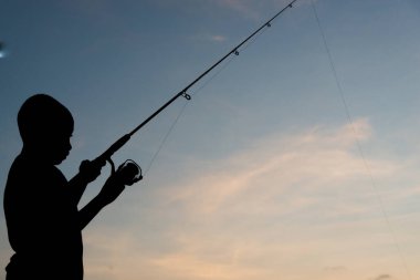 Salvador, Bahia, Brazil - November 16, 2019: Child, in Silhouette, is seen fishing during sunset in the city of Salvador, Bahia. clipart