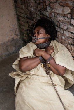 Ağzında demir bir maske olan, zincirlenmiş, Pelourinho 'da duvara yaslanmış siyah bir kadın. Brezilya 'da kölelik. Köle Anastacia 'yı temsil ediyorum..