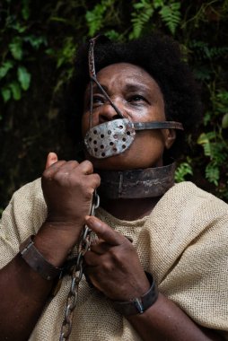 Ağzında ve boynunda demir bir maskeyle köle gibi giyinmiş ve ellerini tutan bir kadının portresi. Brezilya 'da kölelik. Köle Anastacia 'nın temsilcisi.