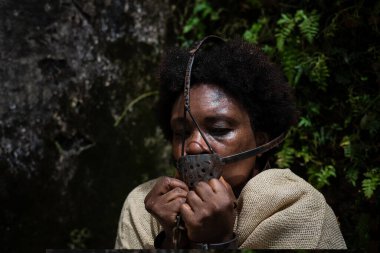 Ağzında ve boynunda demir bir maskeyle köle gibi giyinmiş ve ellerini tutan bir kadının portresi. Brezilya 'da kölelik. Köle Anastacia 'nın temsilcisi.