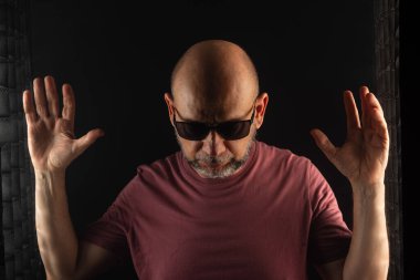 Kel ve sakallı adam, elleri havada güneş gözlüğü takıyor. Koyu dumanlı arka planda izole edilmiş. Güney Amerikalı..