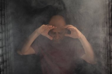 Kel ve sakallı bir adam stüdyoda siyah arka planda duman içinde hareketler ve ifadeler yapıyor. Güney Amerika