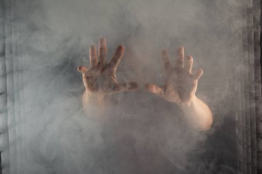 Yoğun dumanların arasında beliren beyaz bir adamın elleri. Siyah arkaplanı olan bir stüdyo resmi. Güney Amerikalı..