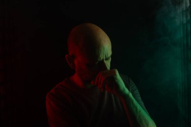 Fotoğraf için poz veren kel ve sakallı bir adam. Koyu dumanlı arka planda, renkli ışıklarla izole edilmiş. Güney Amerikalı..