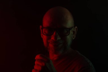 Fotoğraf için poz veren kel ve sakallı bir adamın yakın plan portresi. Koyu dumanlı arka planda, renkli ışıklarla izole edilmiş. Güney Amerikalı..