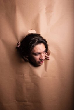 Adamın kafası kağıttan bir delikten sarkıyor ve elleri kağıdı bir kenara itiyor. Stüdyo resmi.
