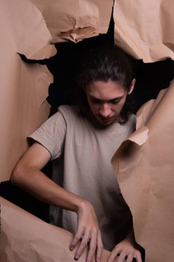 Kahverengi bir kağıt parçasındaki delikten bakan bir adam. Gazeteyi elleriyle yırttı. Stüdyo resmi.