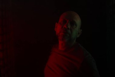 Fotoğraf için poz veren kel ve sakallı bir adam. Koyu dumanlı arka planda, renkli ışıklarla izole edilmiş. Güney Amerikalı..