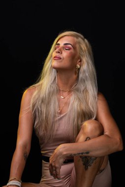 Salvador, Bahia, Brezilya - 18 Ekim 2024: somon rengi elbise giyen sarışın kadın tahta taburede oturmuş fotoğraf için poz veriyor. Siyah arka planda izole edilmiş. Salvador, Bahia.