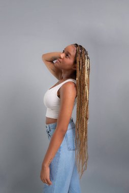 Saçında örgüler olan güzel esmer bir kadının portresi yukarı bakıyor. Sakin ve kendinden emin. Gri stüdyo arka planında izole edilmiş..