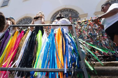 Salvador, Bahia, Brazil - January 16, 2025: Catholics are seen tying ribbons to the fence during the washing of Bonfim in the city of Salvador, Bahia. clipart