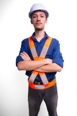 Beyaz kasklı ve parlak yelek giyen genç mimar kollarını kavuşturmuş fotoğraf için poz veriyor. Beyaz arka planda izole edilmiş. Güvenlik ekipmanları.