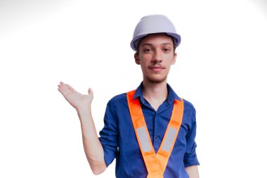 Beyaz kasklı ve parlak yelek giyen genç mimar fotoğraf için poz veriyor ve el hareketi yapıyor. Beyaz arka planda izole edilmiş. Güvenlik ekipmanları.