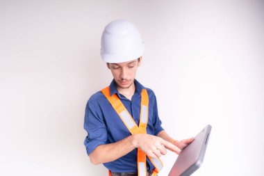 Genç mimar beyaz kask ve parlak yelek giyiyor, dizüstü bilgisayarla çalışıyor. Beyaz arka planda izole edilmiş. Güvenlik ekipmanları.