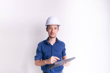 Beyaz kask ve parlak yelek giyen genç bir mimar dizüstü bilgisayar tutuyor ve kameraya bakıyor. Beyaz arka planda izole edilmiş. Güvenlik ekipmanları.