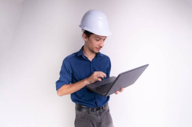 Genç mimarın portresi beyaz kask takıyor, dizüstü bilgisayarla çalışıyor. Beyaz arka planda izole edilmiş. Güvenlik ekipmanları.