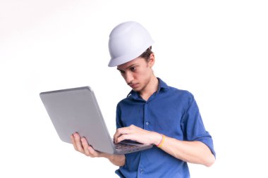 Genç mimarın portresi beyaz kask takıyor, dizüstü bilgisayarla çalışıyor. Beyaz arka planda izole edilmiş. Güvenlik ekipmanları.