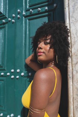 Siyah saçlı, sarı elbiseli güzel bir zenci kadın büyük yeşil kilise kapısına poz veriyor. Mutlu ve gülümsüyor