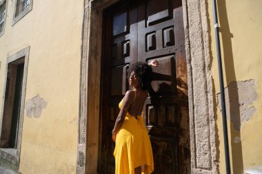 Sarı elbiseli güzel bir kadının portresi eski kahverengi ahşap kapının yanında duruyordu. Mutlu insan seyahat konsepti.