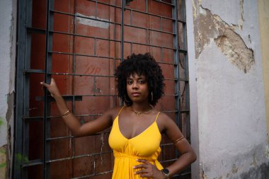 Sarı elbiseli, afro saçlı güzel bir kadın elinde kırmızı kapılı demir bir korkuluk tutuyor. Yolculukta kendine güveni olan biri.