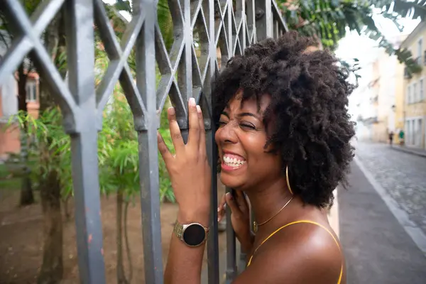 Eski demir bir çite dayanan sarı bir elbise giyen afro saçlı güzel siyah bir kadının portresi. Yolculuktaki mutlu insan..