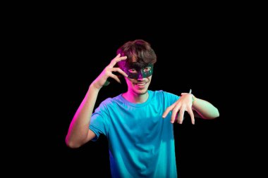 Karnaval maskesi takan yakışıklı genç adam kameraya bakıp el hareketi yapıyor. Siyah arka planda izole edilmiş. Brezilya