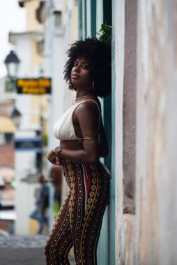 Arkası duvara dönük, fotoğraf için poz veren güzel siyahi bir kadının yarım boy fotoğrafı. Gülümseyen ve güçlü bir insan. Brezilya