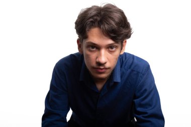 Siyah saçlı ve mavi gömlekli yakışıklı bir gencin yakın plan portresi, kameraya ciddi ciddi bakıyor. Beyaz arka planda izole edilmiş. Kendine güvenen biri. Profesyonel konsept.